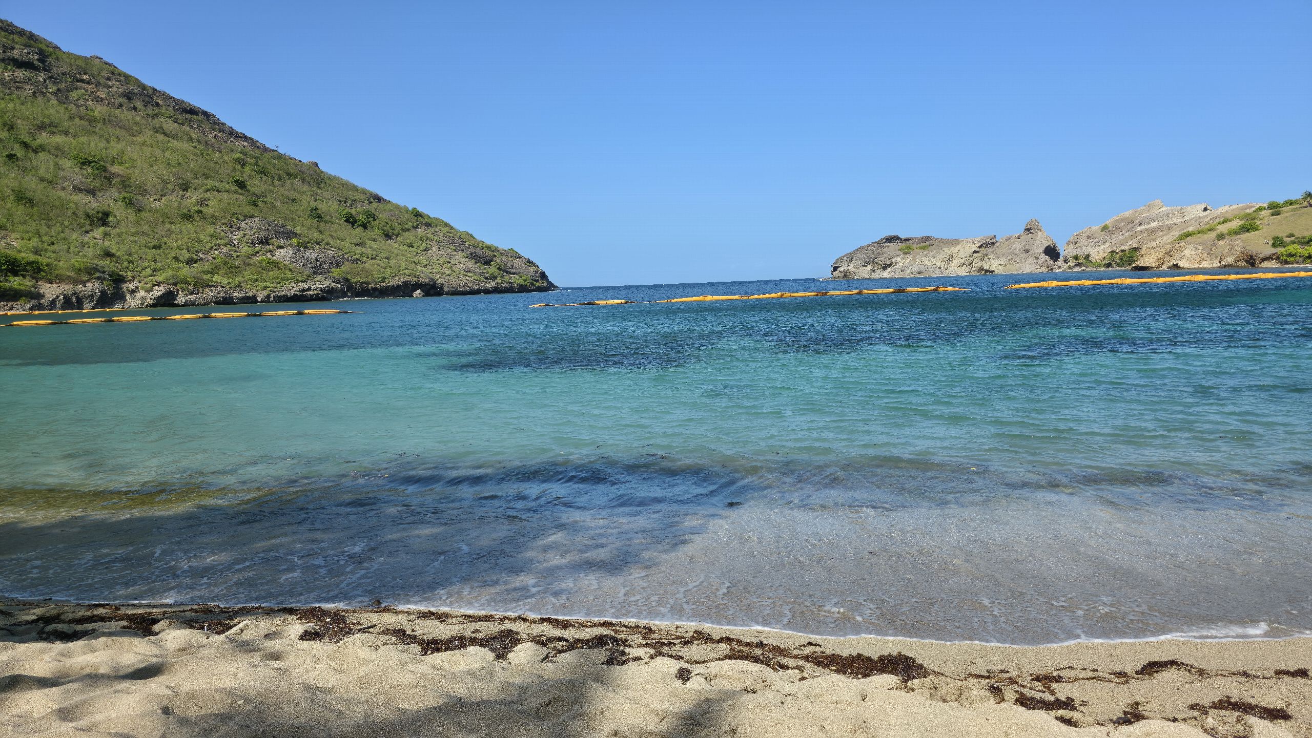 Crique aux eaux transparentes et au sable clair, bordée de rochers volcaniques